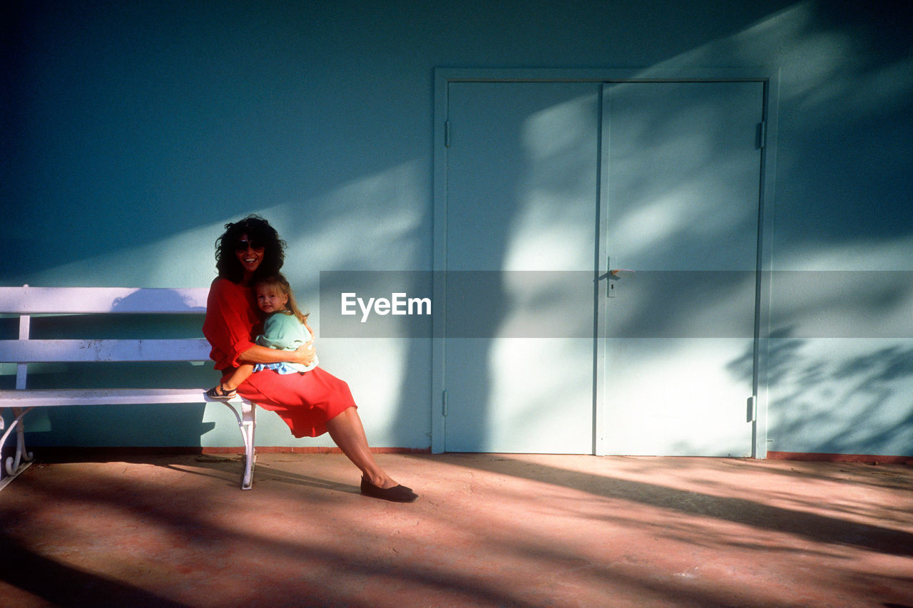 Full length of woman sitting with daughter on bench