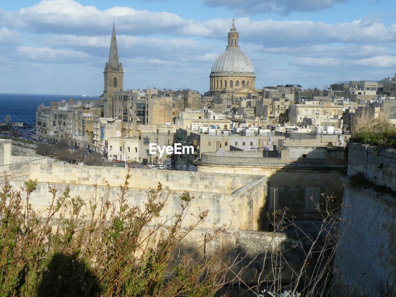 Basilica by buildings in city against cloudy sky