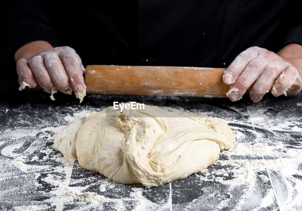 Midsection of person preparing dough against black background