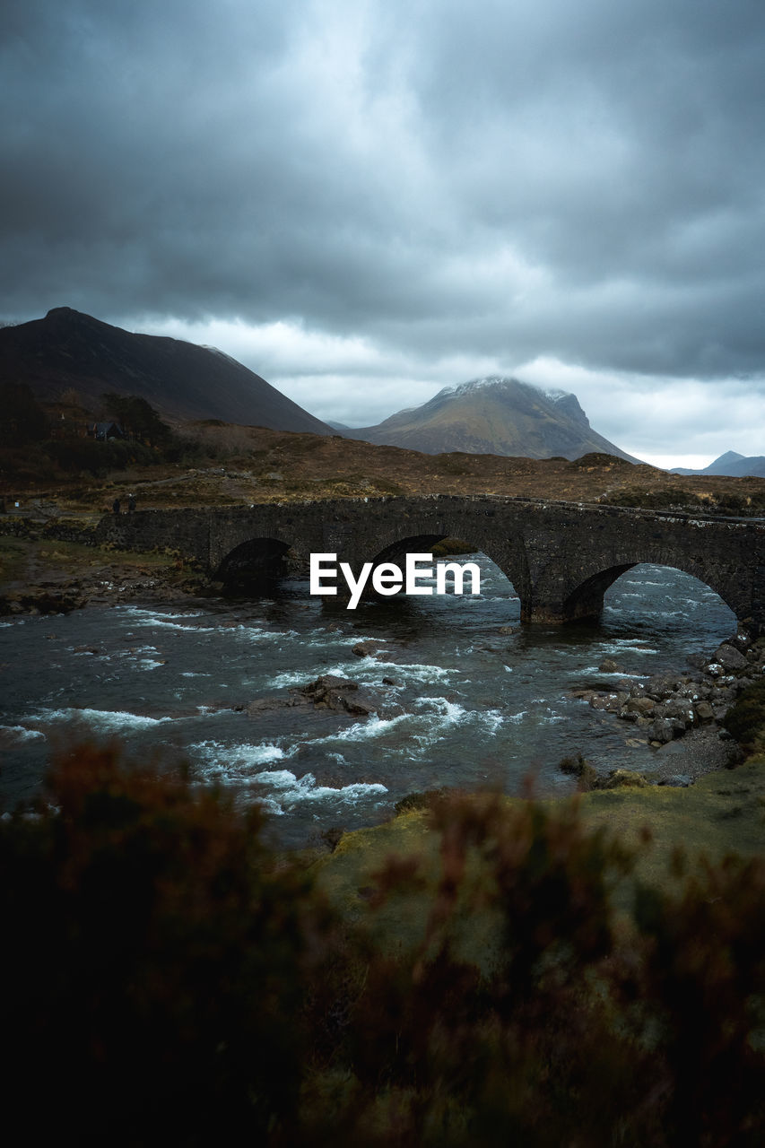 Arch bridge over river against cloudy sky