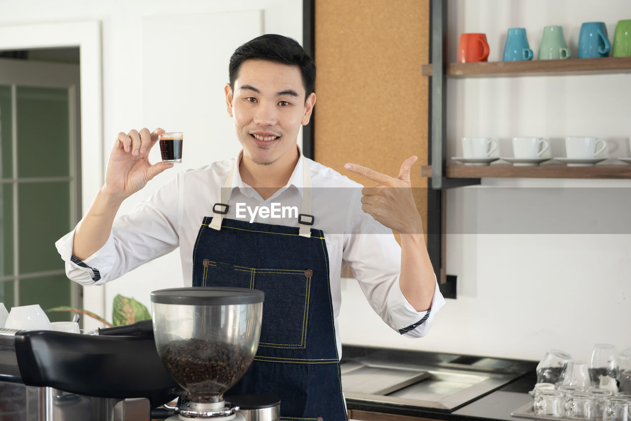 Asian barista man holding and show cup of hot black coffee for customer in the coffee shop