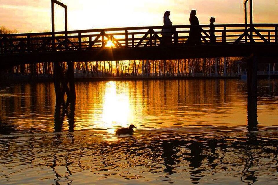 water, reflection, sunset, sky, evening, silhouette, nature, bridge, architecture, dusk, built structure, transportation, beauty in nature, sun, sunlight, river, tranquility, outdoors, pier, men, orange color, scenics - nature, travel destinations, group of people, railing, tranquil scene, cloud, animal themes