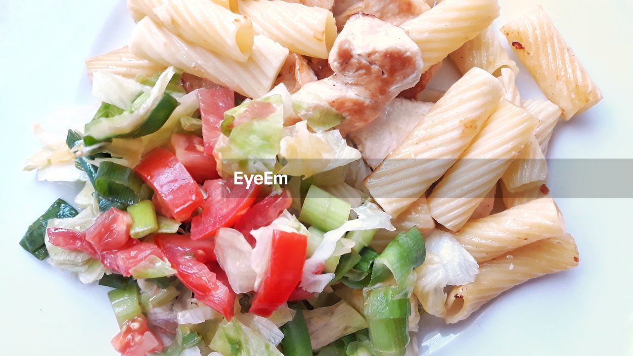 Top view close-up of tortiglioni noodles with chicken meat and iceberg mixed lettuce salad.