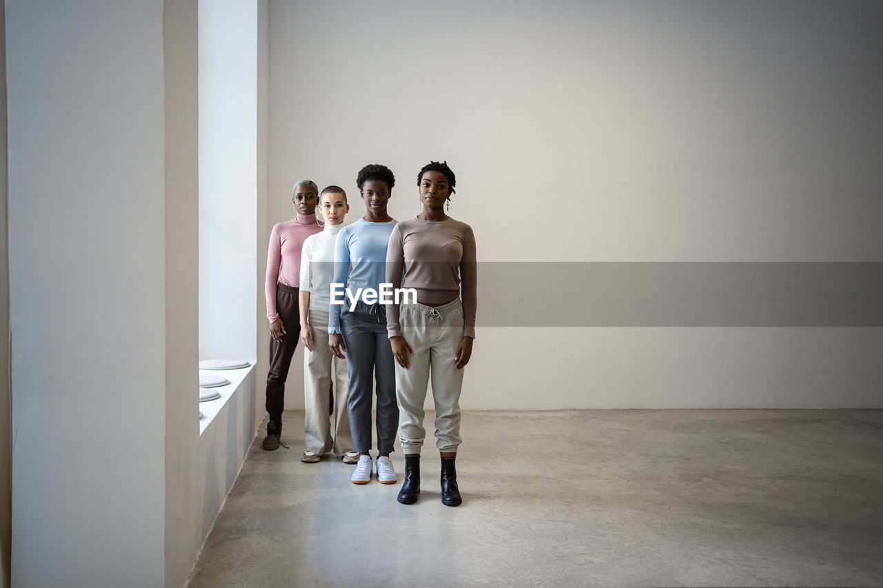 Female friends standing in row against wall at home