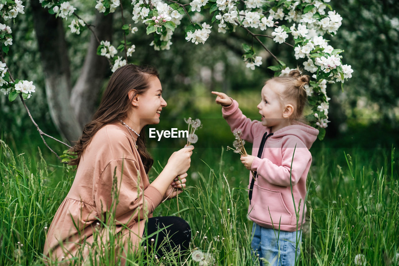 Mother and daughter with dandelions blooming apple trees