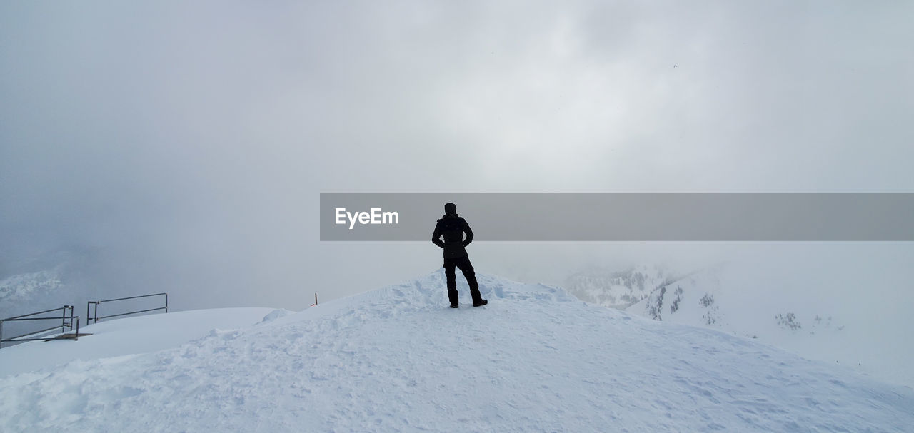 REAR VIEW OF PEOPLE ON SNOWCAPPED MOUNTAIN AGAINST SKY