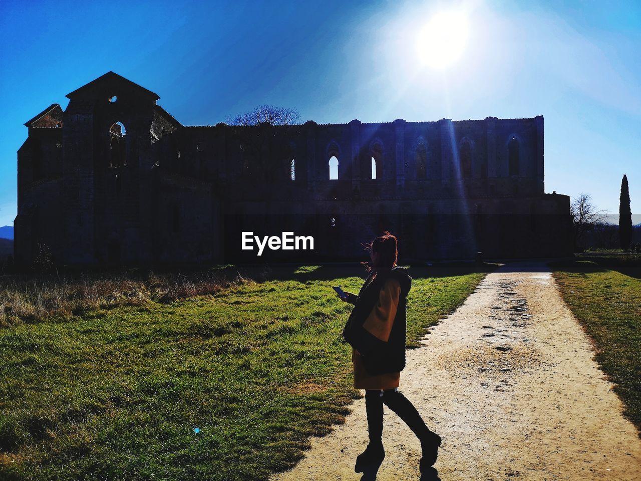 REAR VIEW OF WOMAN WALKING ON FIELD AGAINST BUILDINGS