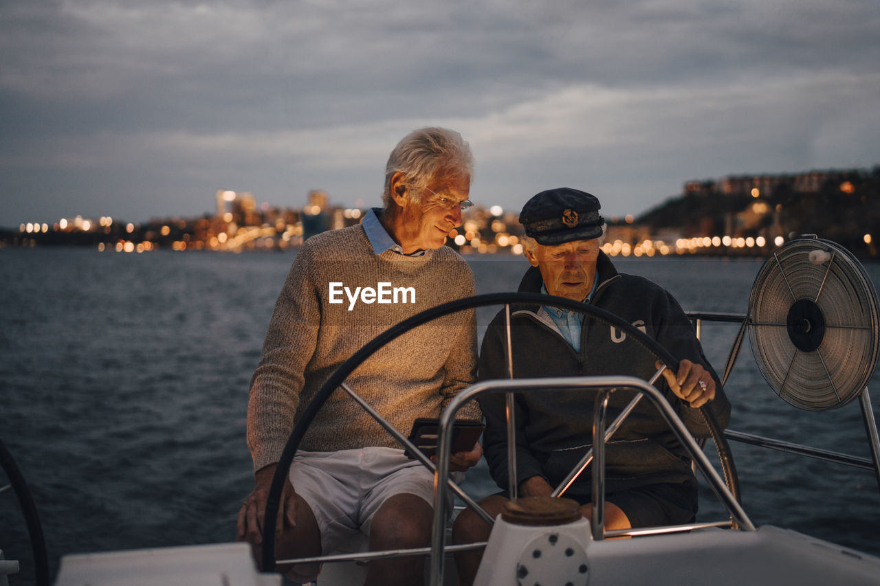 Senior man guiding male friend while sailing boat during sunset