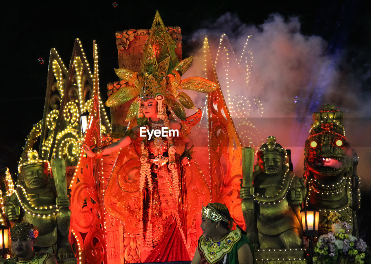 People wearing costumes by sculptures during carnival at night