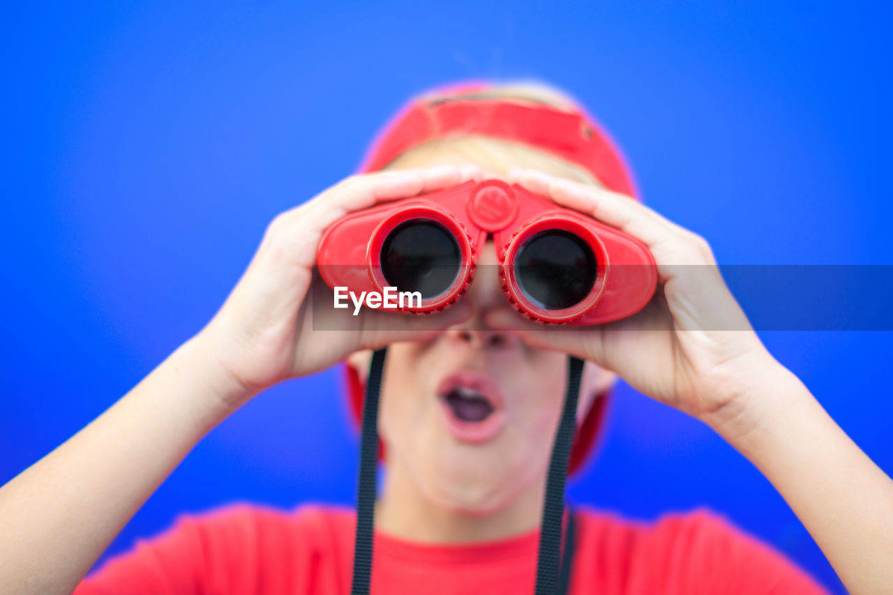 Close-up of boy looking through binoculars against blue background