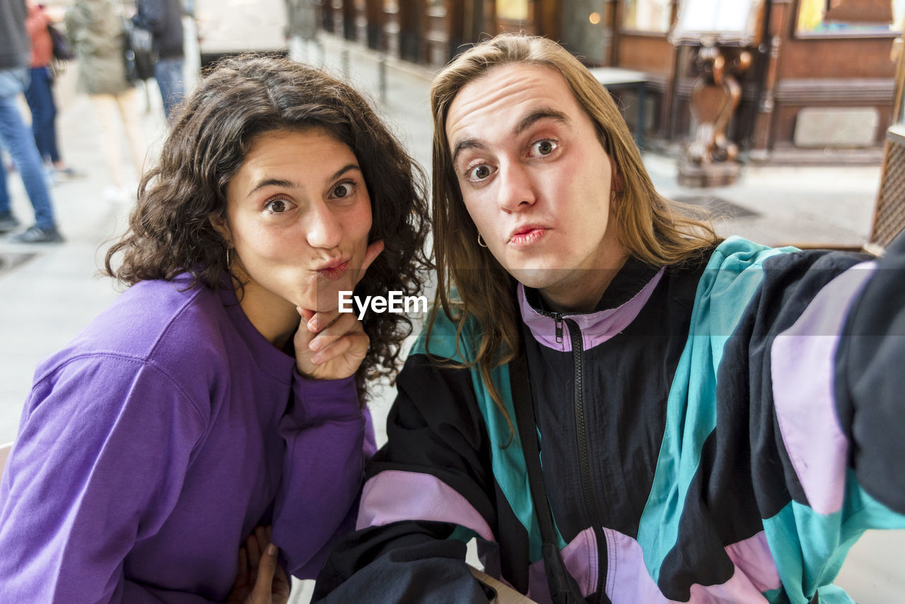 Two friends taking a selfie while sitting on a table outdoors.