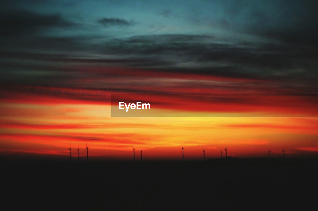 Scenic view of silhouette windmills on field against orange cloudy sky during sunset