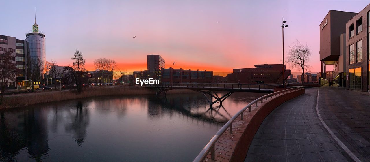 BRIDGE OVER RIVER AGAINST BUILDINGS AT DUSK