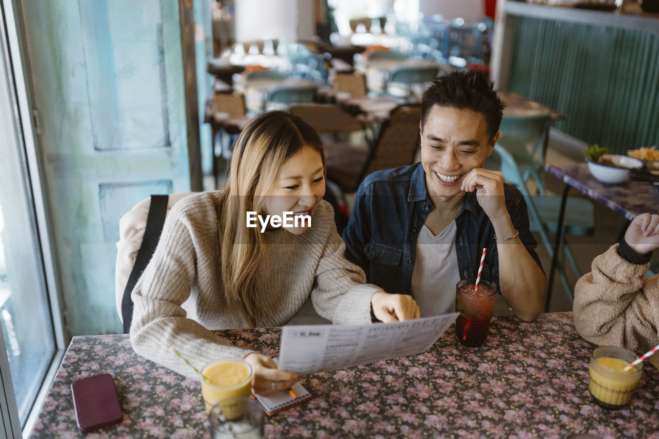 Smiling male and female friends reading menu while sitting together at restaurant