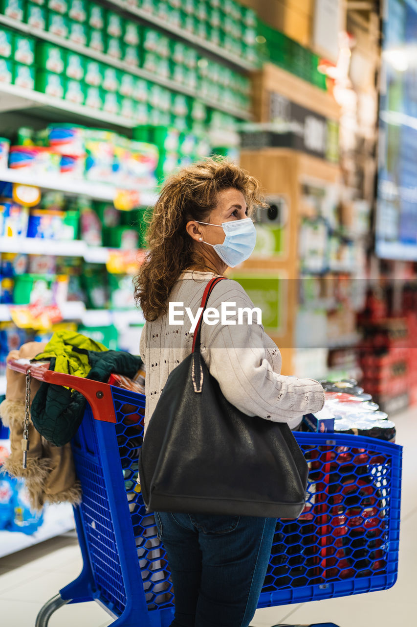 Side view of woman wearing mask standing at shopping mall