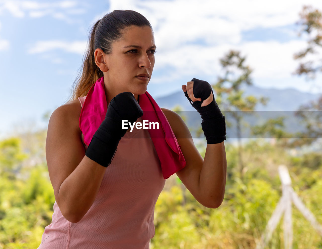 YOUNG WOMAN WITH ARMS RAISED STANDING AGAINST BLURRED BACKGROUND