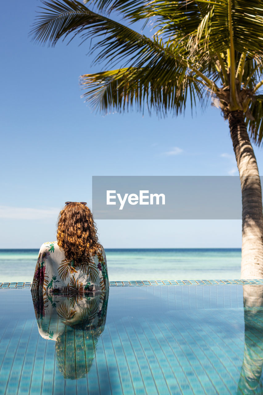 Relaxed woman into a infinity swimming pool looking the ocean