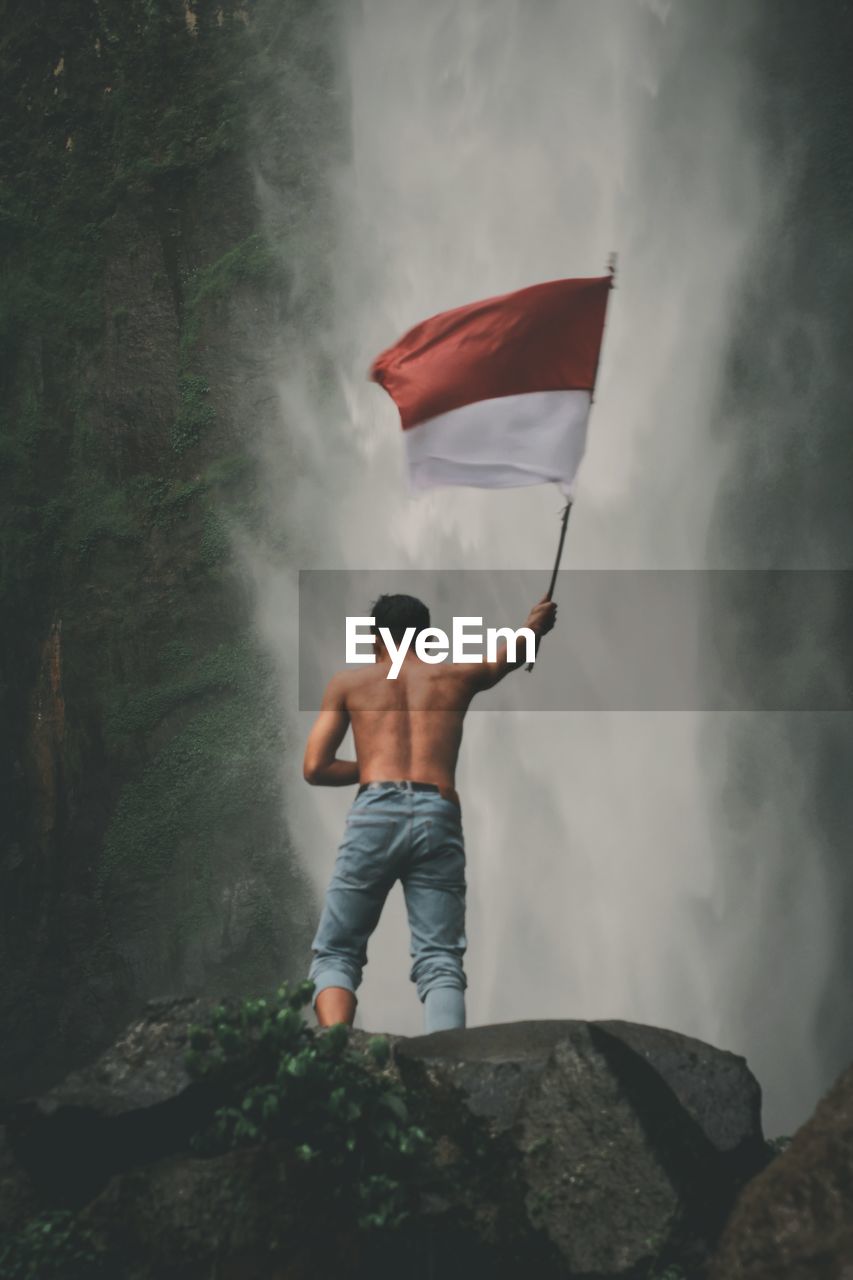 Rear view of man standing on rock with indonesian national flag
