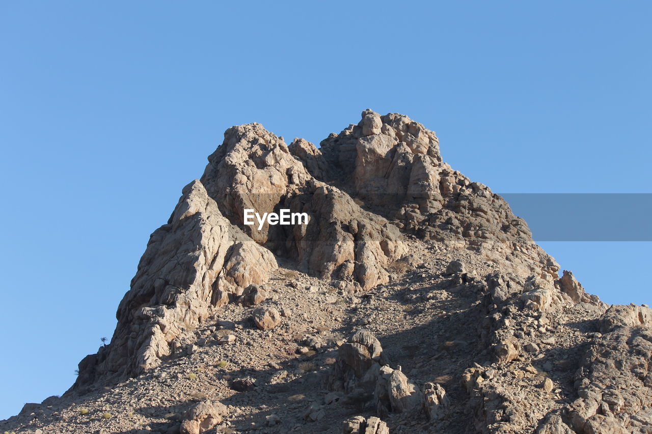 LOW ANGLE VIEW OF ROCKS AGAINST CLEAR BLUE SKY