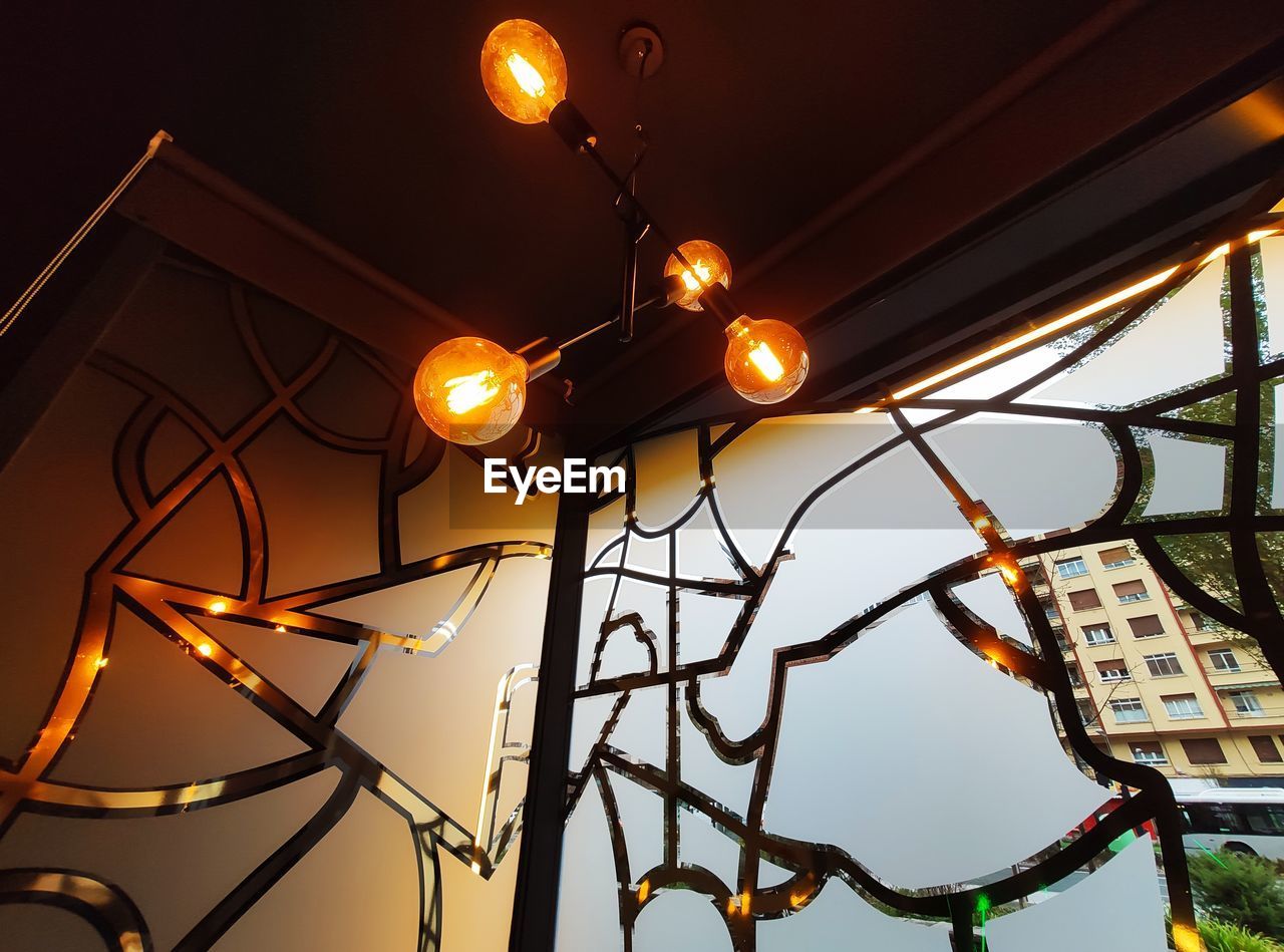 LOW ANGLE VIEW OF ILLUMINATED LIGHT BULBS HANGING FROM CEILING IN BUILDING