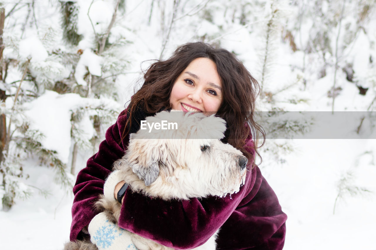 Portrait of smiling woman embracing dog in snow covered forest