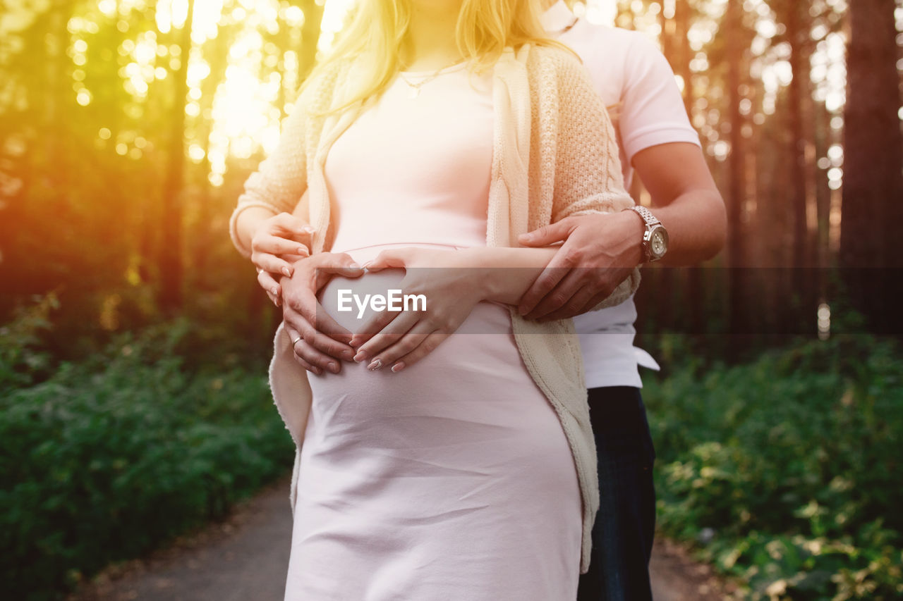 Midsection of man with pregnant wife making heart shape on belly