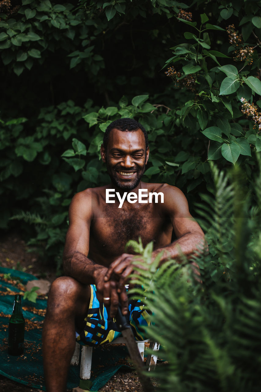 Shirtless man smiling while sitting in yard