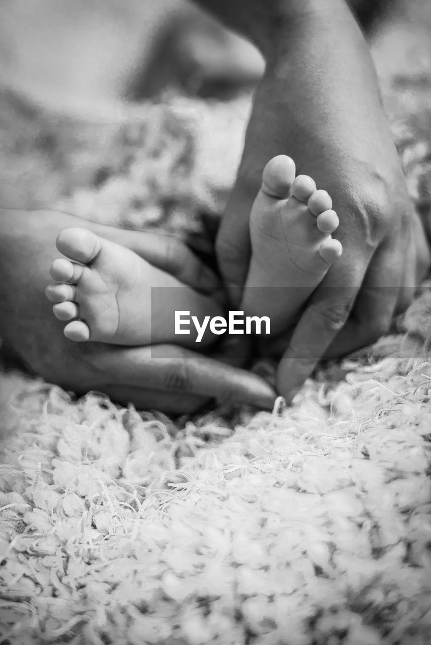 Cropped image of mother holding baby feet on bed