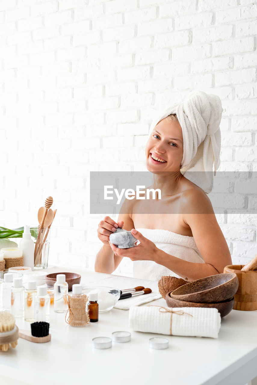 Woman wearing white bathrobes towels on head doing spa procedures mixing natural ingredients