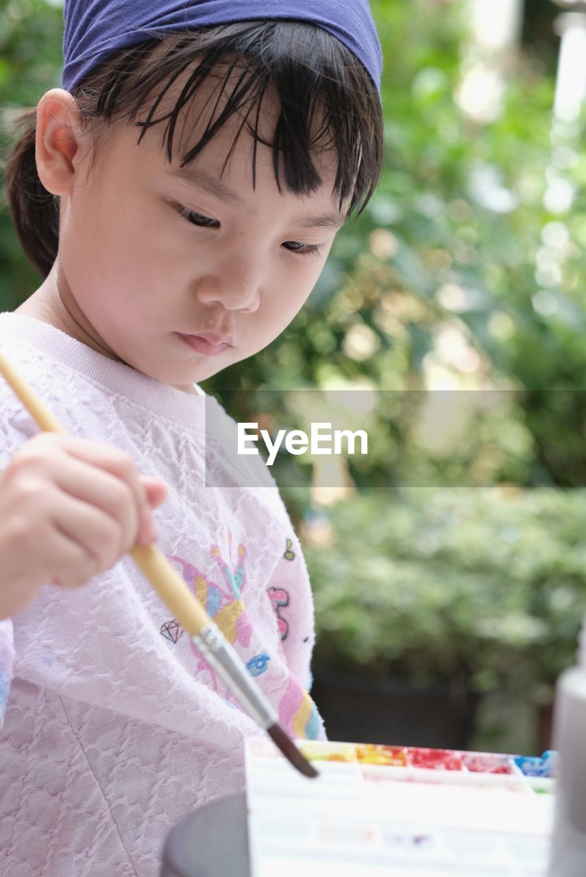 Cute asian child girl is holding paintbrush and painting on the paper. selective focus