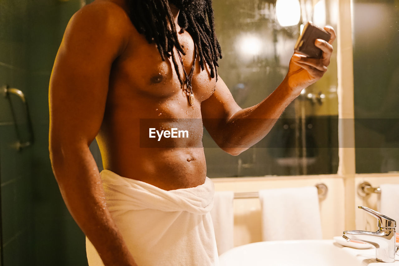 Midsection of shirtless man using phone while standing in bathroom