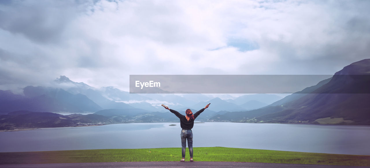 one person, arm, mountain, sky, limb, adult, cloud, beauty in nature, water, human limb, nature, scenics - nature, arms raised, environment, lake, tranquility, standing, leisure activity, tranquil scene, landscape, exercising, vacation, full length, trip, mountain range, arms outstretched, holiday, lifestyles, women, yoga, idyllic, rear view, sports, reflection, relaxation, spirituality, wellbeing, day, vitality, travel, outdoors, solitude, religion, land, young adult, zen-like, meditating, balance, travel destinations, harmony