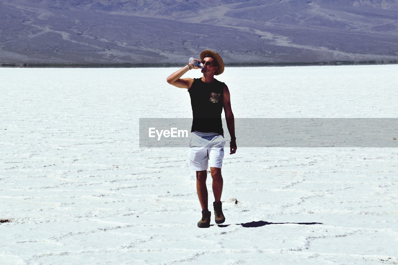 FULL LENGTH OF YOUNG WOMAN STANDING ON LAND AGAINST SEA