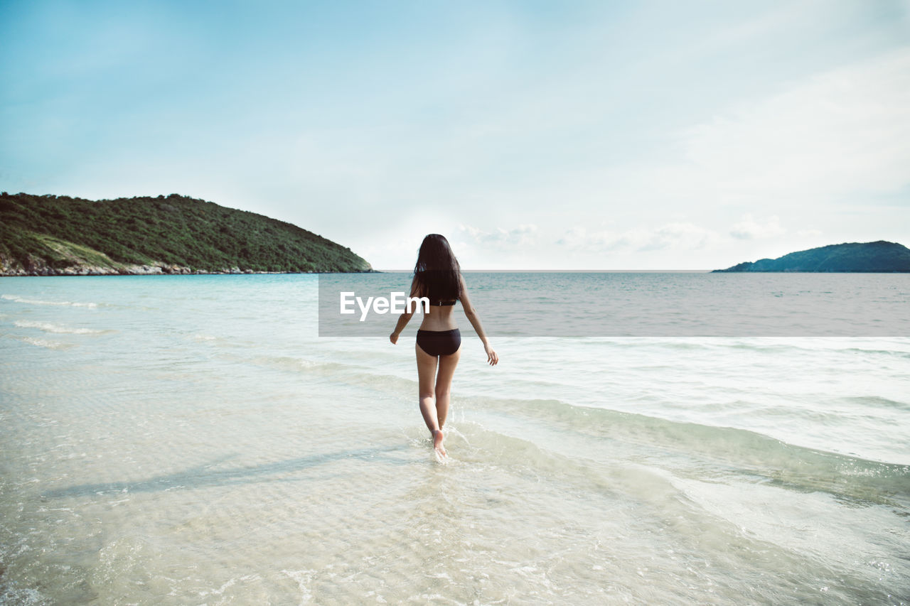 Rear view of woman wearing bikini walking at beach