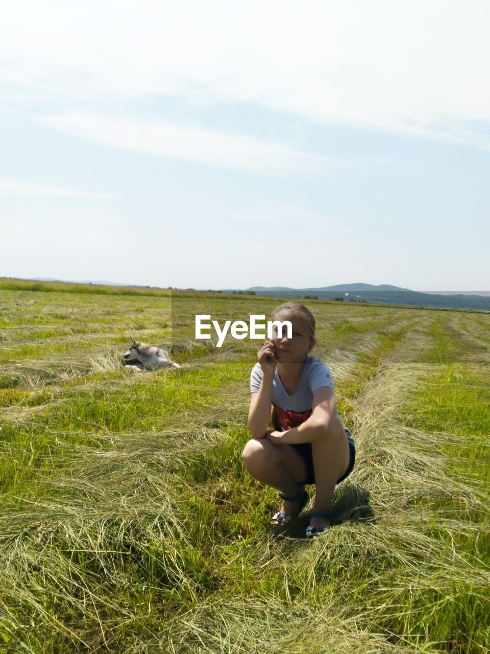 Portrait of girl crouching on grassy land against sky