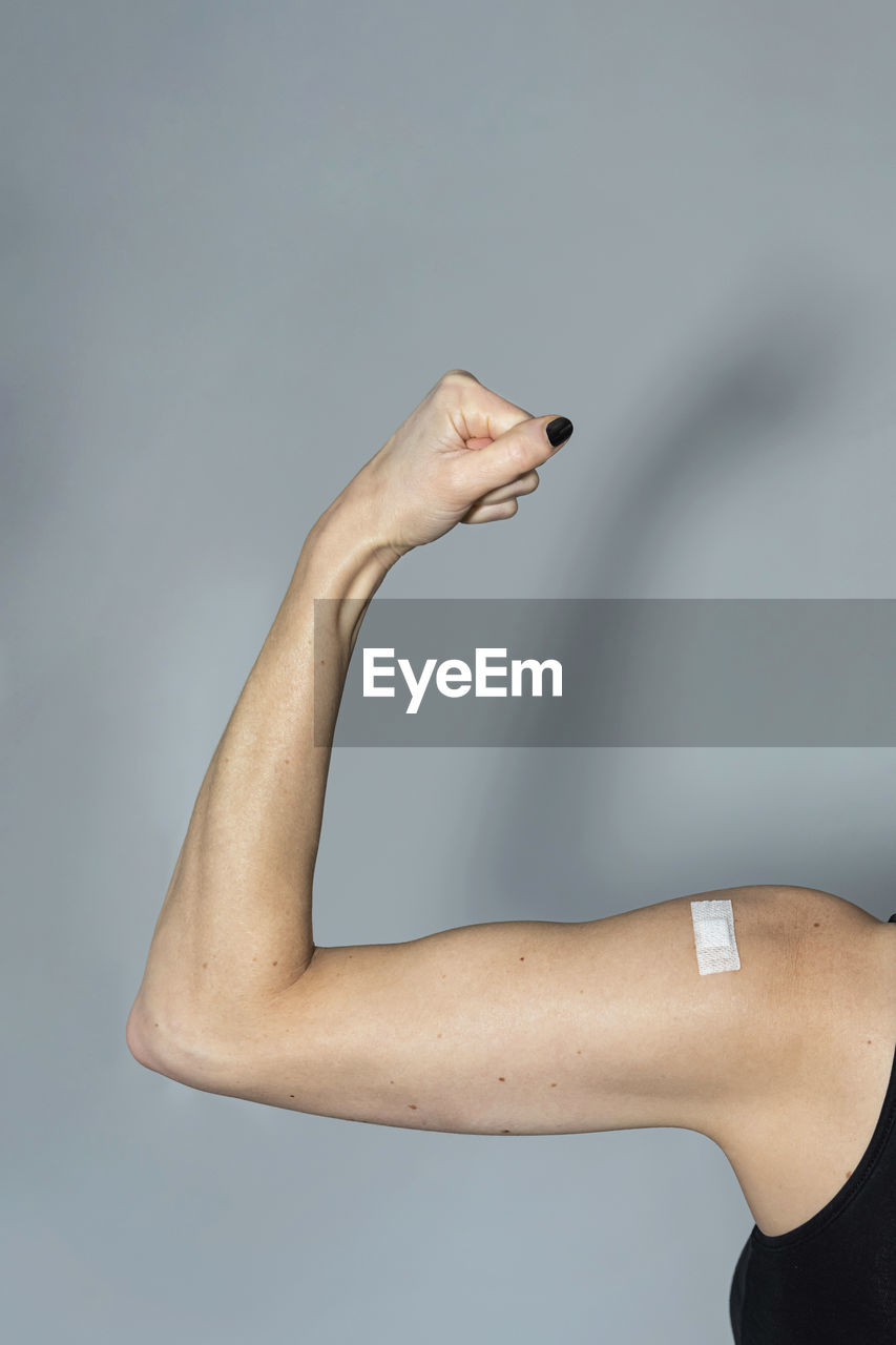 Woman with bandage flexing muscle over gray background