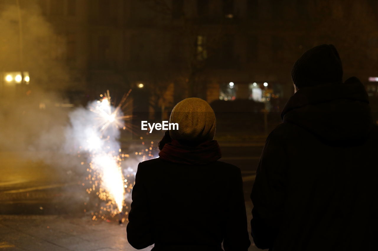 Rear view of people watching firework display at night