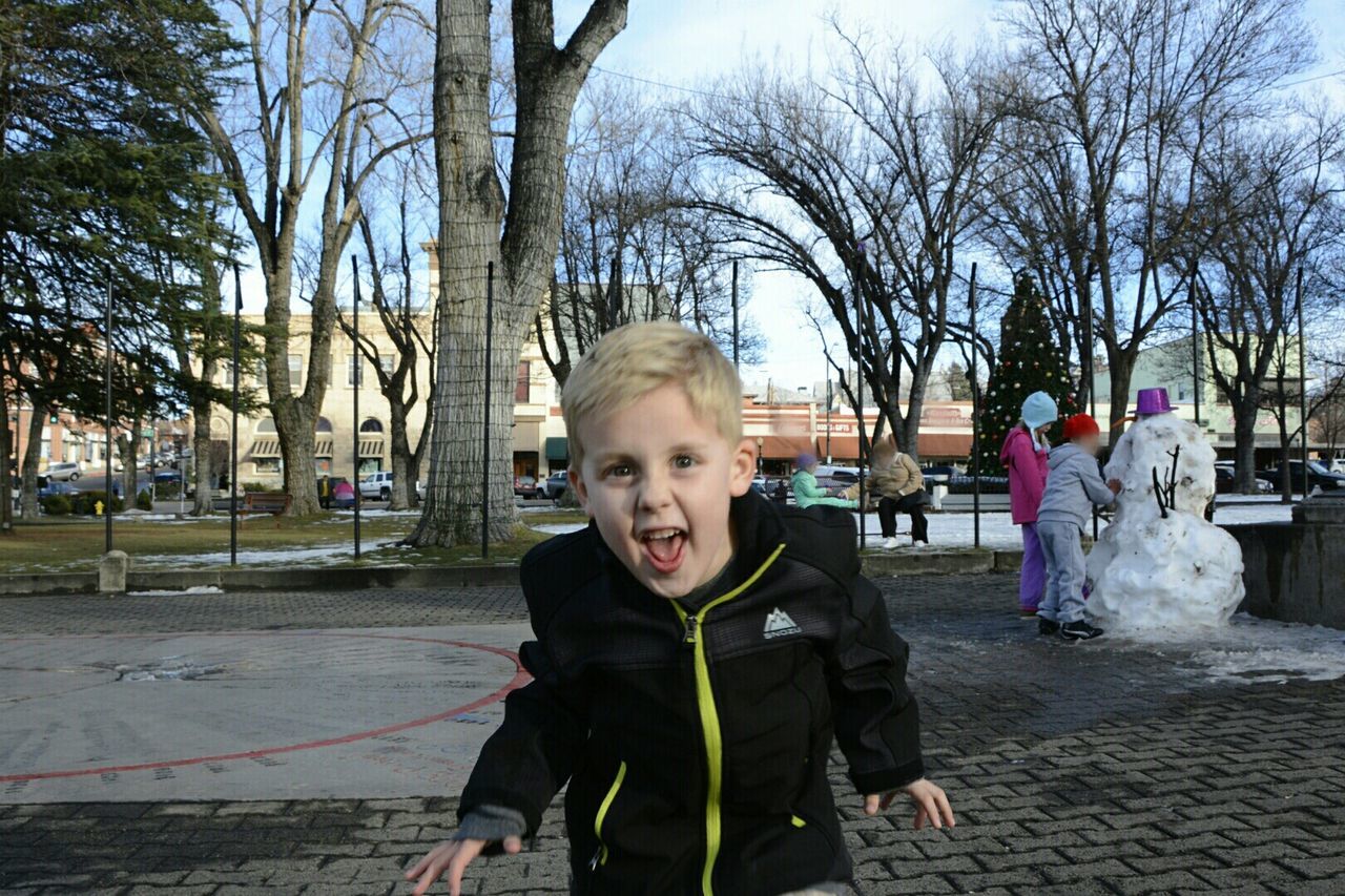 Excited boy shouting while standing on sidewalk against bare trees during winter