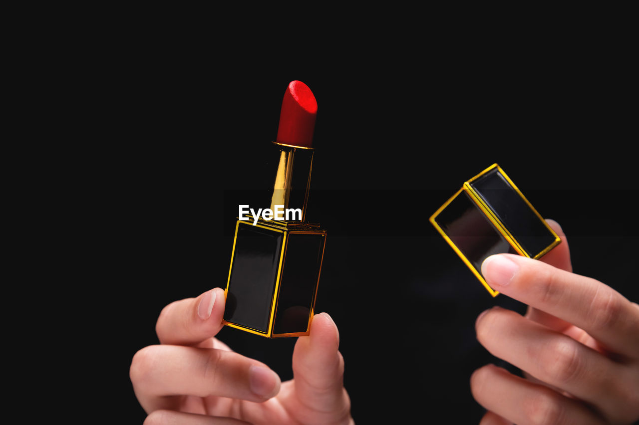 Woman's hand holding a red lipstick in a gold-black frame in one hand, in the other hand a lipstick
