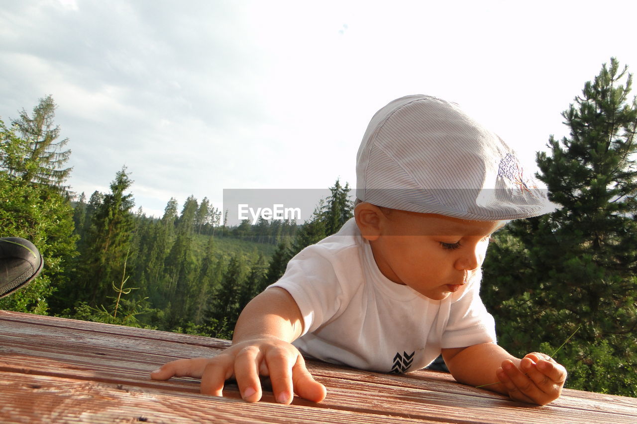 Close-up of boy leaning on wooden table against forest