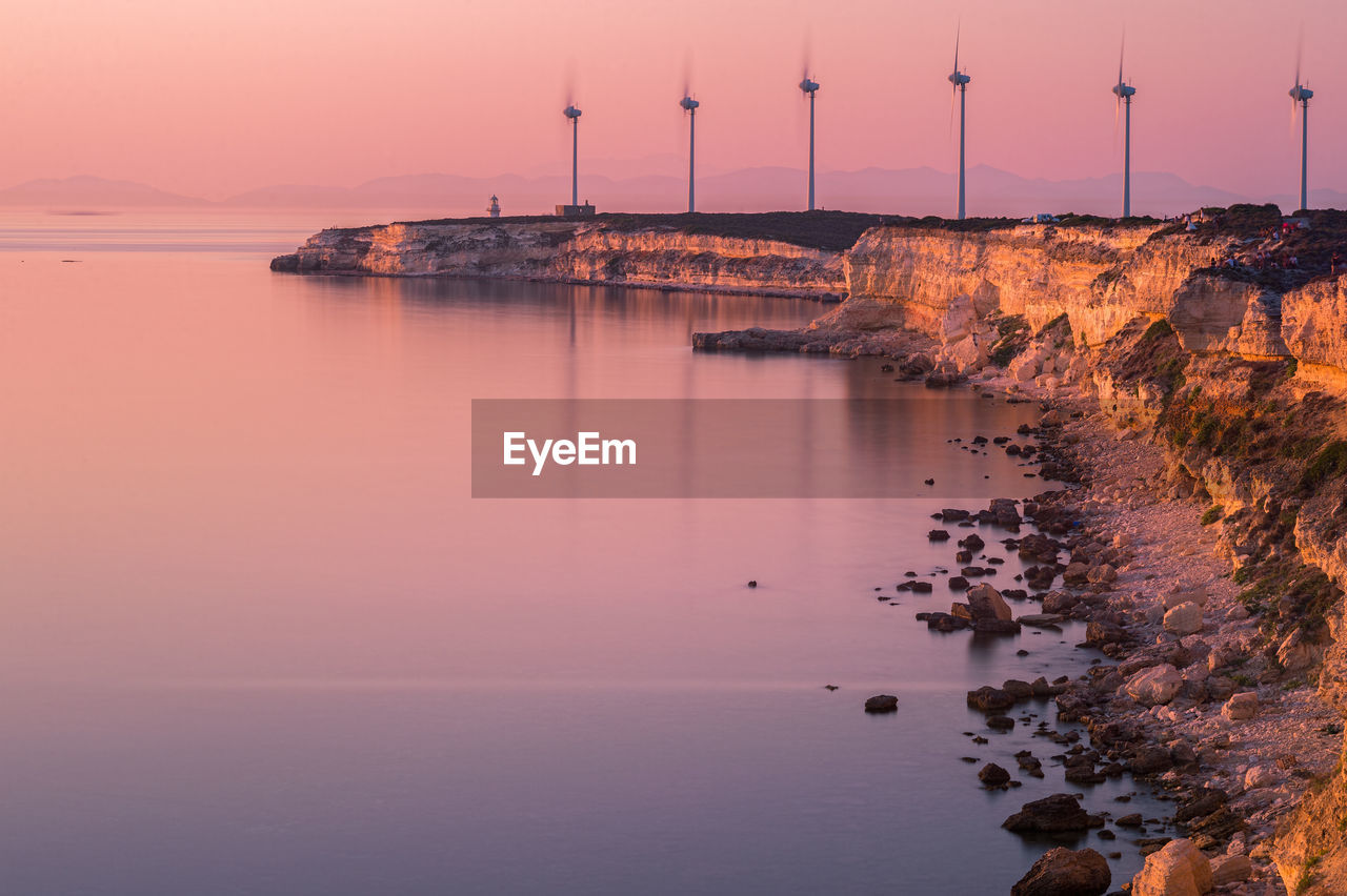 Windmills by sea against sky during sunset