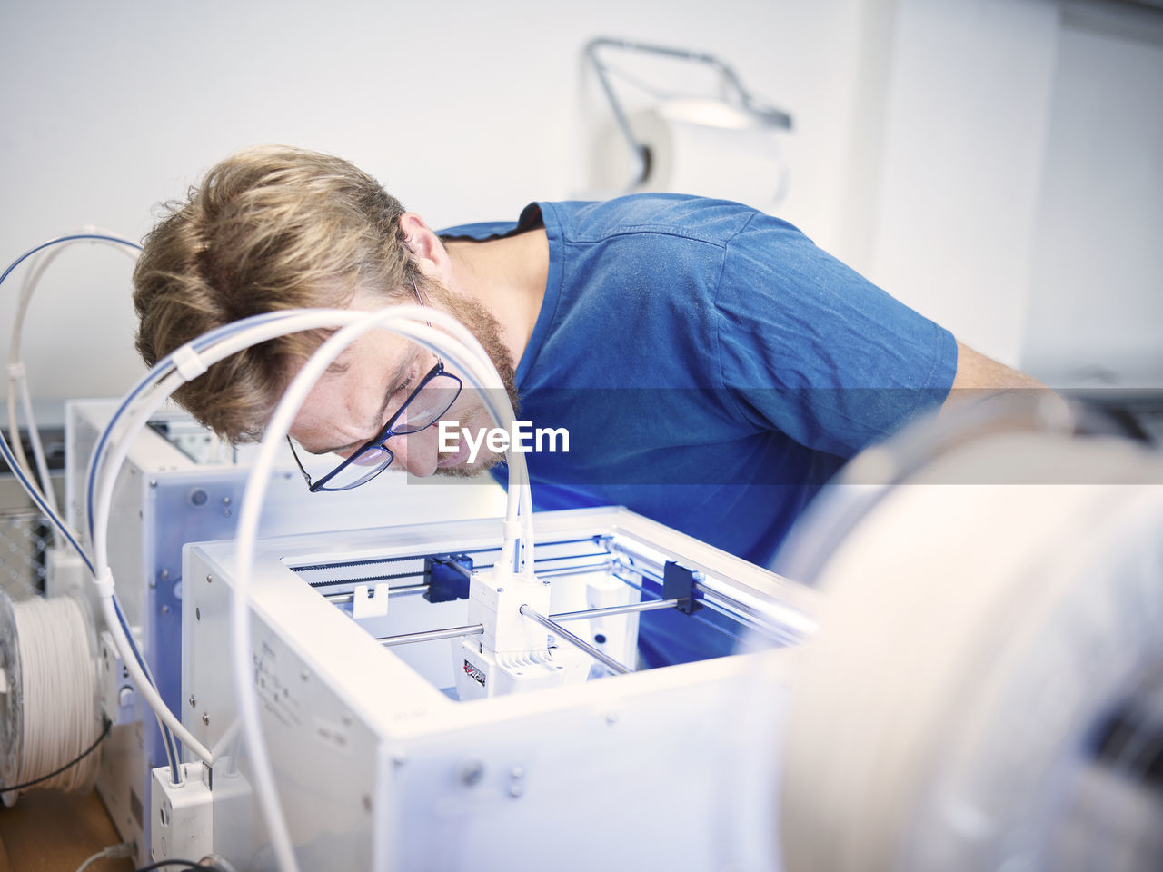 Technician wearing eyeglasses analyzing 3d printer at workshop