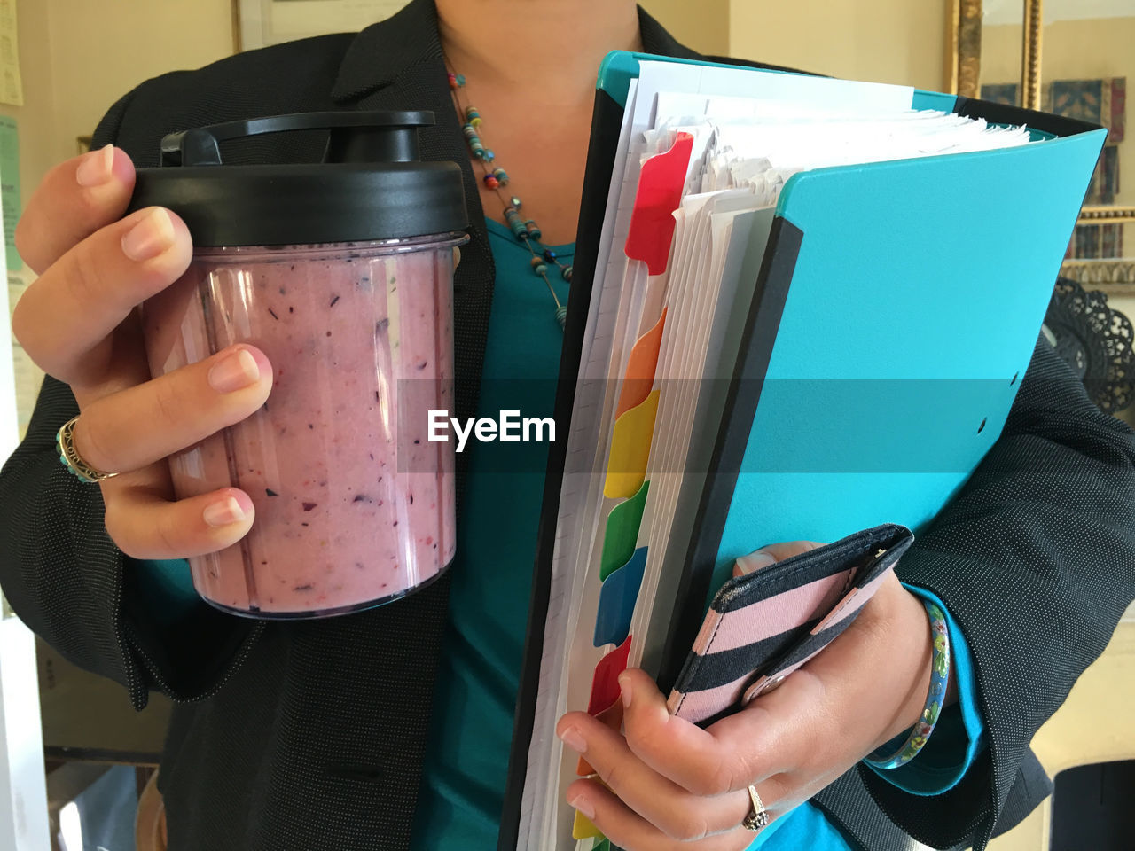 Midsection of businesswoman holding files and smoothie container at home