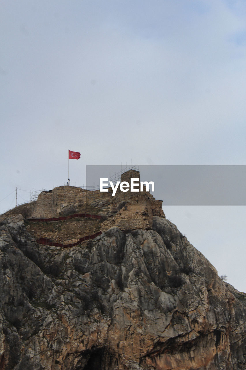 flag, sky, rock, patriotism, mountain, nature, terrain, day, no people, cliff, low angle view, cloud, outdoors, environment, architecture, rock formation, tower, sea, land, travel destinations, coast, built structure, scenics - nature, geology, travel, ridge, summit