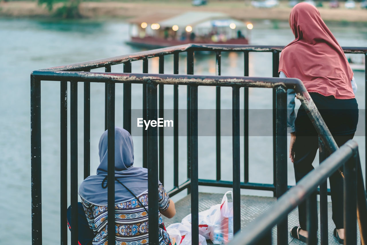 REAR VIEW OF WOMAN STANDING AGAINST RAILING