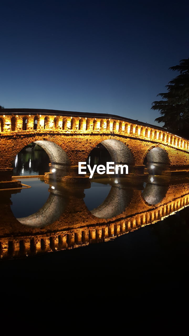 Illuminated bridge over river against sky at night