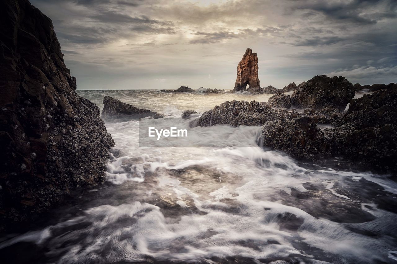 Waves splashing on rocks at shore against sky