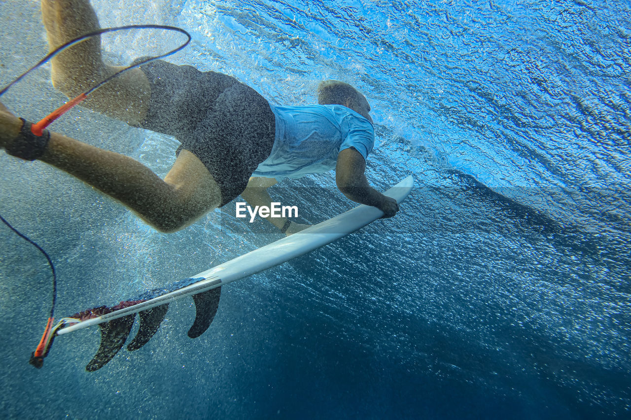 Underwater view of young man surfing in blue waters of south male atoll