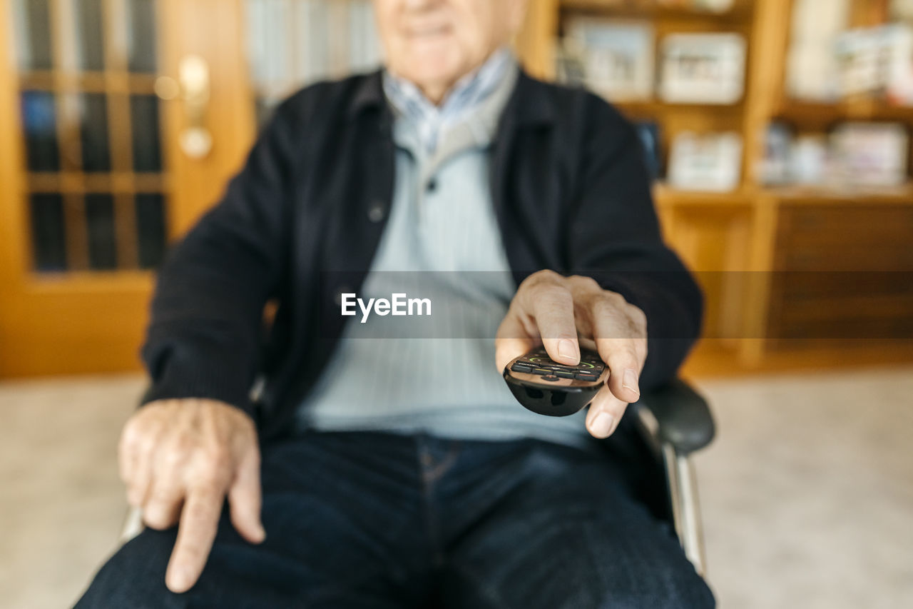 Hand of senior man sitting in wheelchair using remote control, close-up