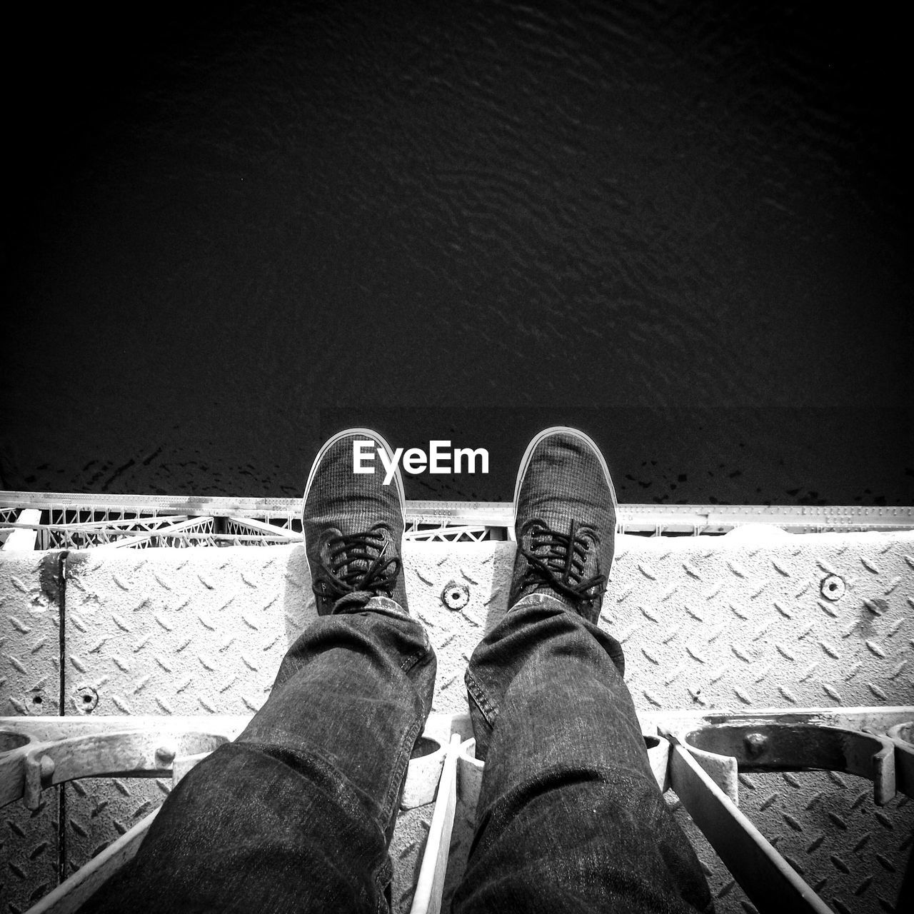 Low section of man standing on metallic bridge over lake